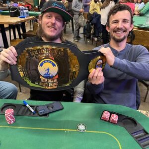 Two men holding up a DEAL CANCER OUT IX-The Golden Ticket belt at a table.