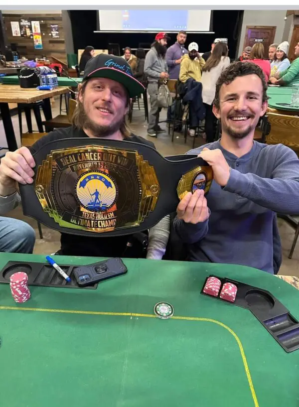 Two men holding up a DEAL CANCER OUT IX-The Golden Ticket belt at a table.