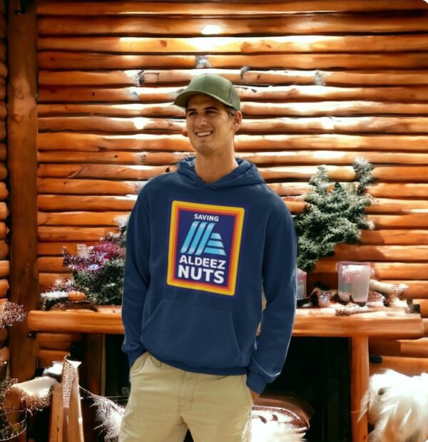 A man wearing an All Deez Nuts- Hoodie stands in front of a log cabin.